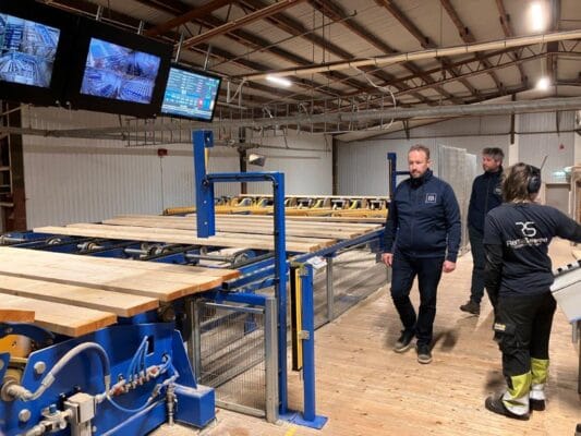 Cursisten zien hoe bij Eksjo hout wordt gesorteerd. Dit gebeurt machinaal en staat op schermen boven de productielijn.